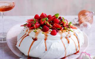 Side view of a dome shaped pavlova with strawberries, raspberries and syrup on top