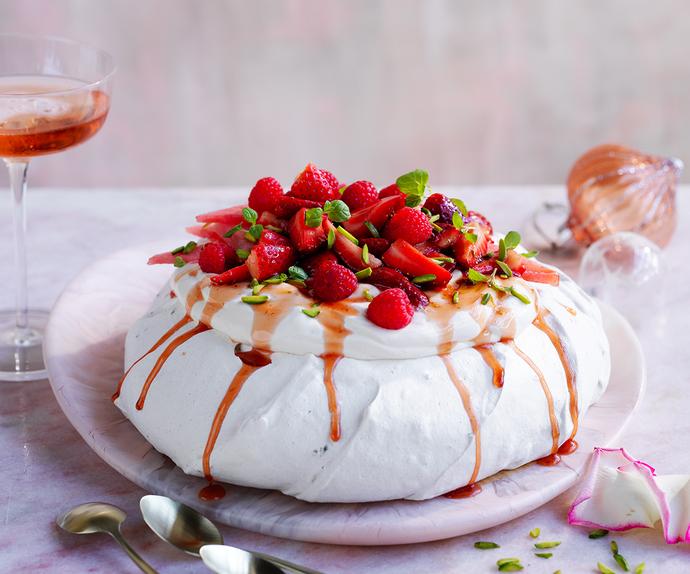 Side view of a dome shaped pavlova with strawberries, raspberries and syrup on top