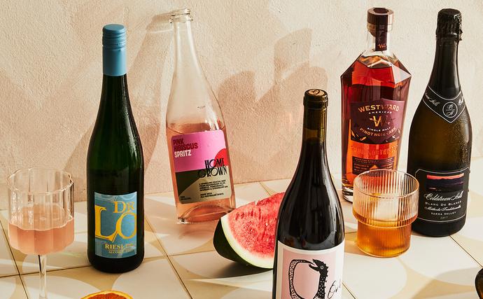 best summer drinks guide. photo of a pale backdrop and a line-up of bottles, glasses and cans showcasing beverage picks