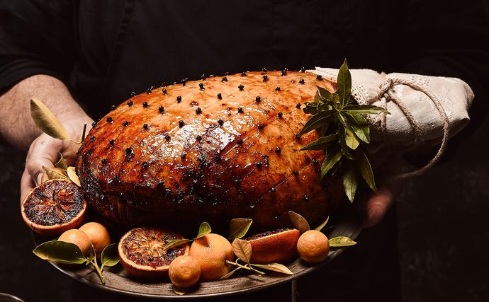 Best christmas hams australia to buy - glazed christmas ham on platter, surrounded by halved blood oranges and whole orange cirtus